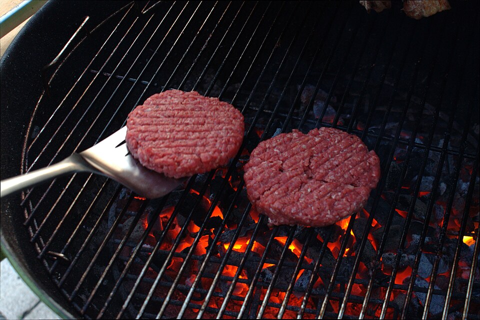 Burger Patties being grilled on a BBQ while using a Spatula.