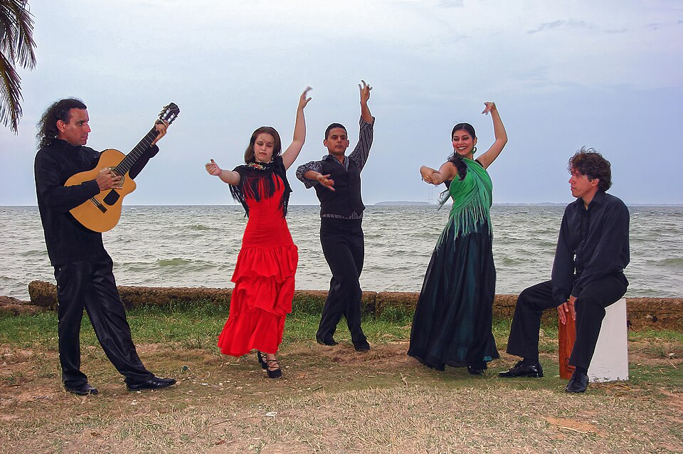 A flamenco group. Singer sits on hollow box (cajón) which he taps with his hands.